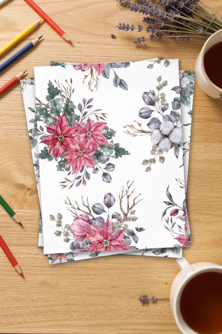 Watercolor Christmas paper with red poinsettia bouquets on white, printed sheets stacked on an oak desk with coloured pencils and a cup of tea
