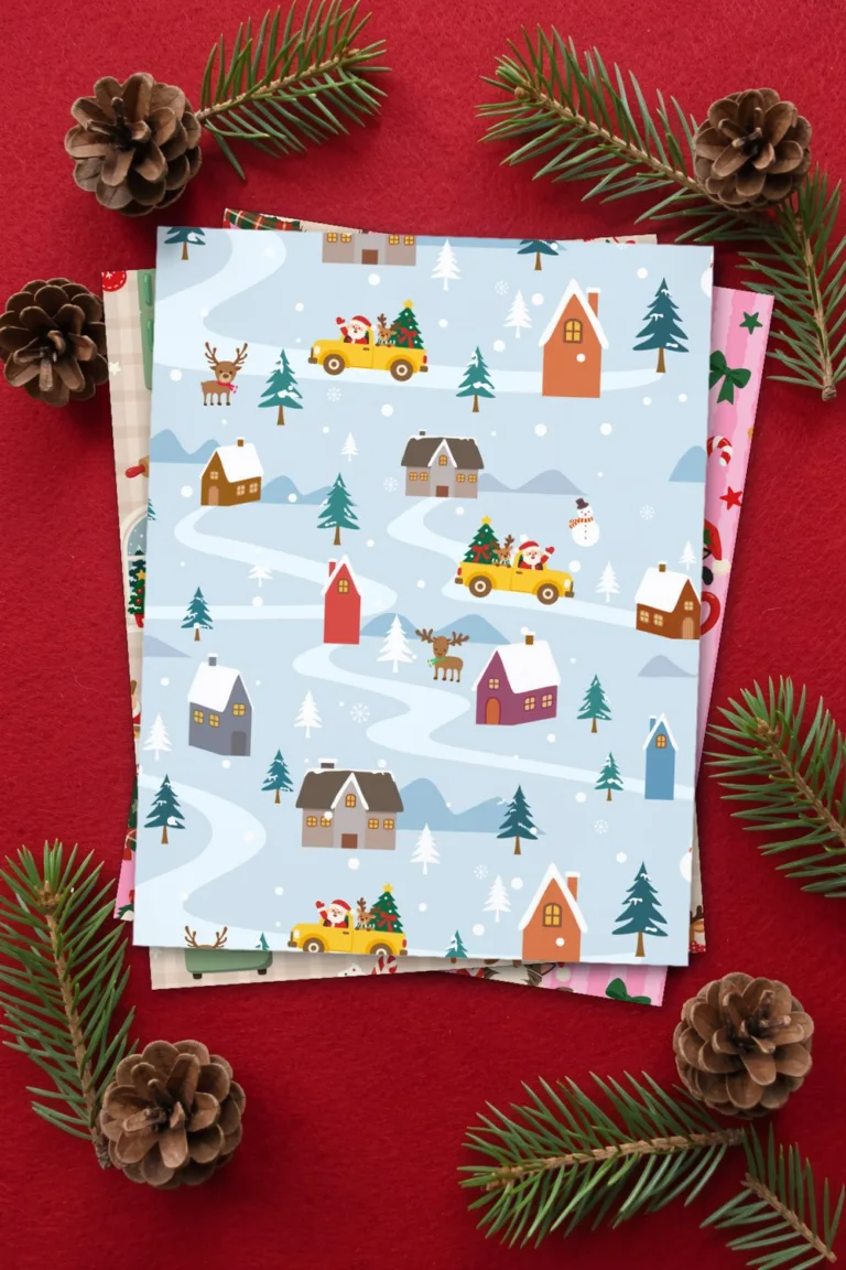 Cute Christmas paper with a snowy village, houses and little cars, printed sheets stacked, on red felt with pine cones and fir sprigs