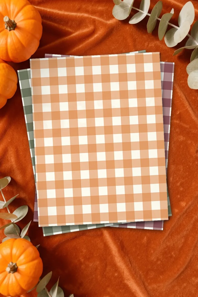 Orange gingham scrapbook paper, printed sheets stacked, on rust orange velvet with small pumpkins and dried eucalyptus