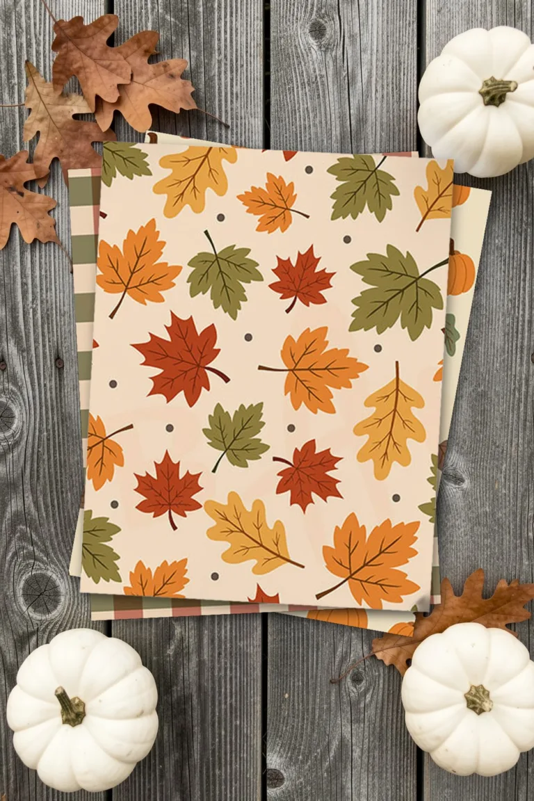 Fall scrapbook paper with maple leaves, printed sheets stacked, on grey barn wood with dried oak leaves and white pumpkins