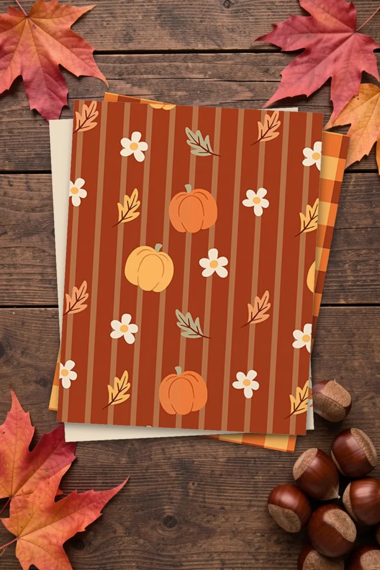 Fall scrapbook paper with pumpkins and flowers on rust, printed sheets stacked, on a dark wooden table with maple leaves and chestnuts