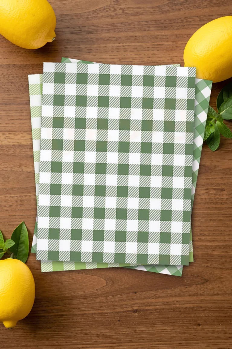 Forest green gingham scrapbook paper, printed sheets stacked, on a brown wooden table with lemons and fresh mint