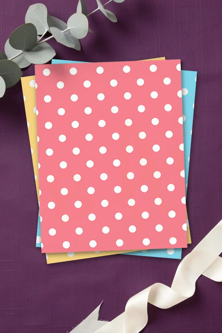 Rose pink polka dot scrapbook paper, printed sheets stacked, on plum purple linen with a eucalyptus branch and an ivory silk ribbon