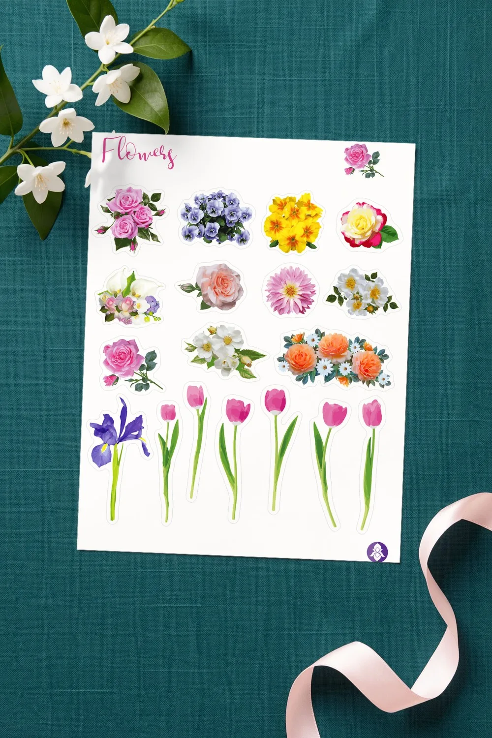 Printed sheet of realistic flower stickers with roses, pansies, a dahlia and pink tulips, on deep teal linen with a branch of white jasmine and a pink silk ribbon