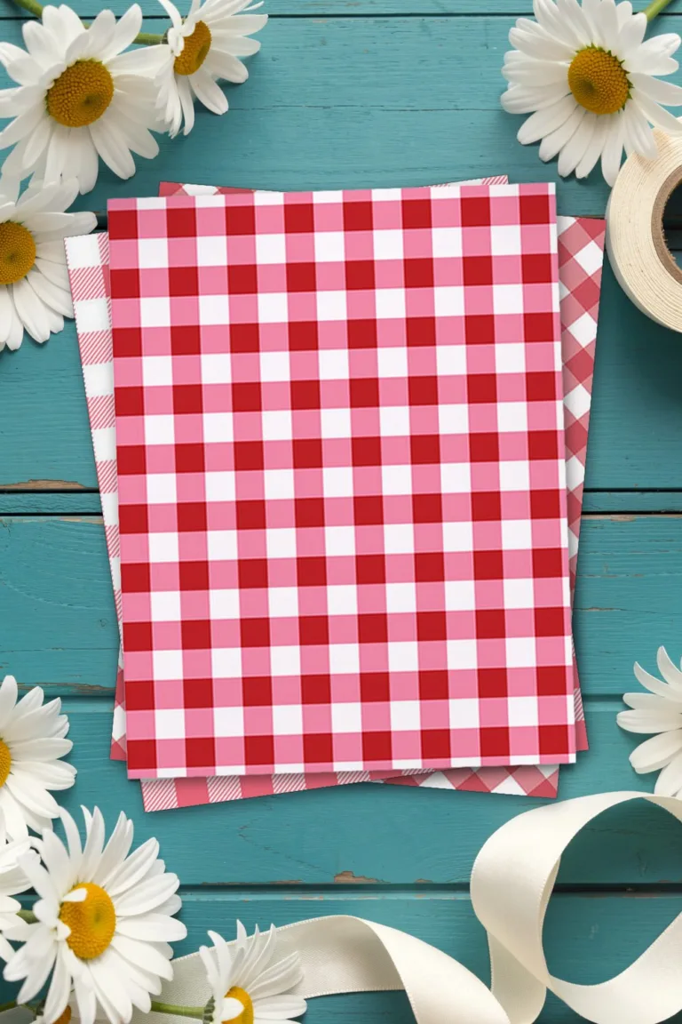 Red gingham scrapbook paper, printed sheets stacked, on teal wooden boards with white daisies and cream ribbon