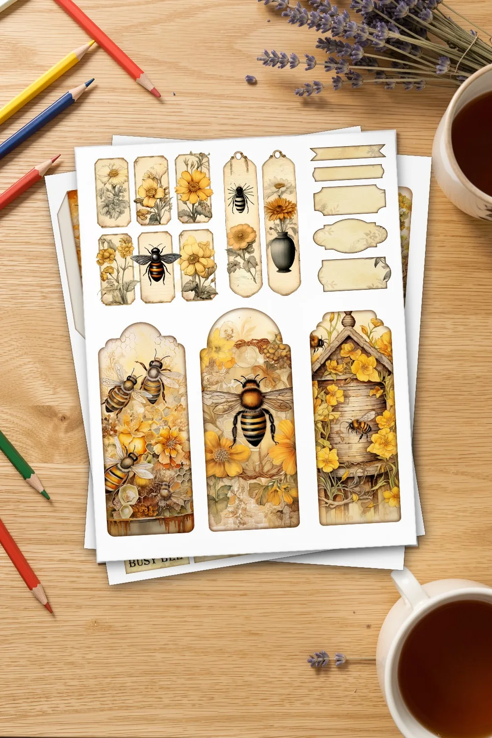 Printed page of bee and flower tags and labels, with pages of cards and pockets under it, on an oak desk with coloured pencils and a cup of tea
